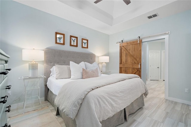 bedroom featuring a barn door, a raised ceiling, and ceiling fan