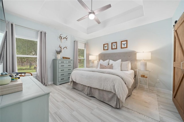 bedroom featuring a barn door, a tray ceiling, and ceiling fan