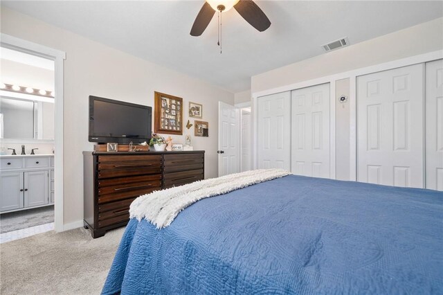 carpeted bedroom featuring ceiling fan, multiple closets, sink, and ensuite bath