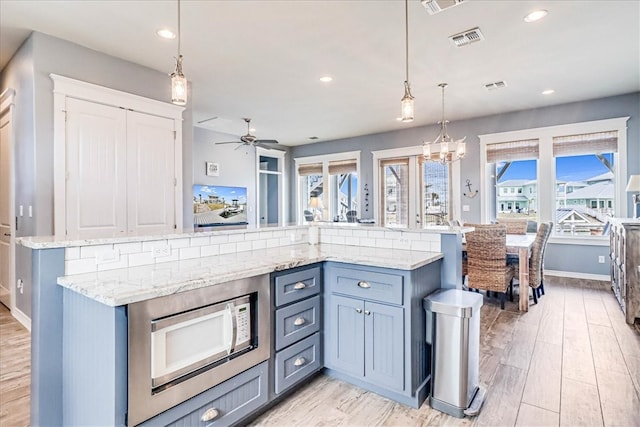 kitchen featuring ceiling fan with notable chandelier, stainless steel microwave, hanging light fixtures, backsplash, and light hardwood / wood-style flooring