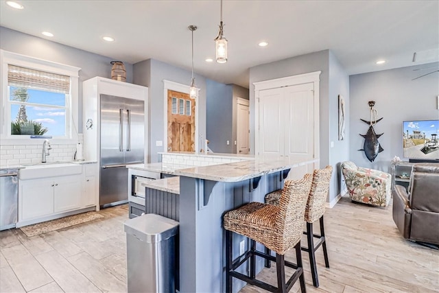 kitchen featuring tasteful backsplash, stainless steel appliances, a kitchen island, white cabinetry, and hanging light fixtures