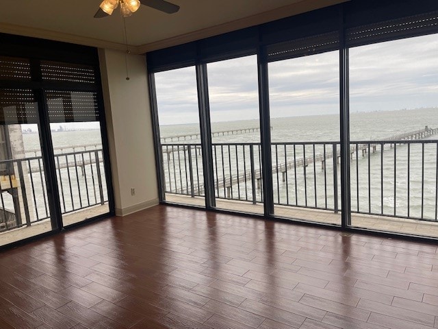 unfurnished room with ceiling fan, a water view, and dark hardwood / wood-style floors