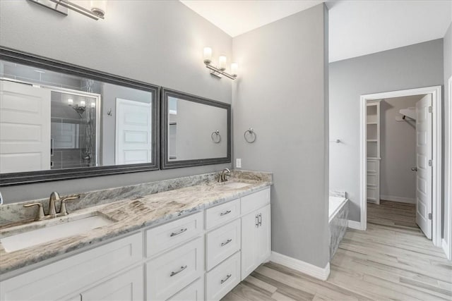 bathroom featuring wood finished floors, double vanity, a walk in closet, a stall shower, and a garden tub