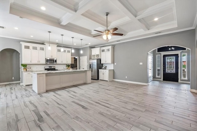 kitchen with appliances with stainless steel finishes, arched walkways, beam ceiling, open floor plan, and light countertops