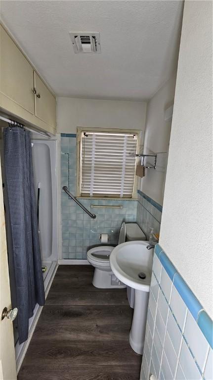 bathroom featuring toilet, walk in shower, hardwood / wood-style floors, and tile walls