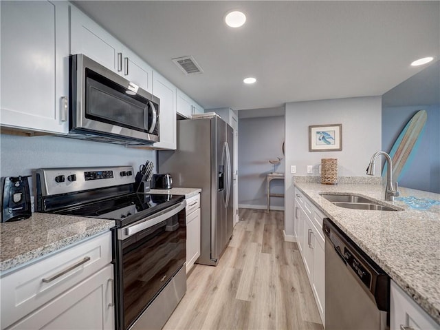 800 Sandcastle Dr Unit 129, Port Aransas, TX 78373 - kitchen featuring appliances with stainless steel finishes, a sink, white cabinets, light stone countertops, and light wood-style floors