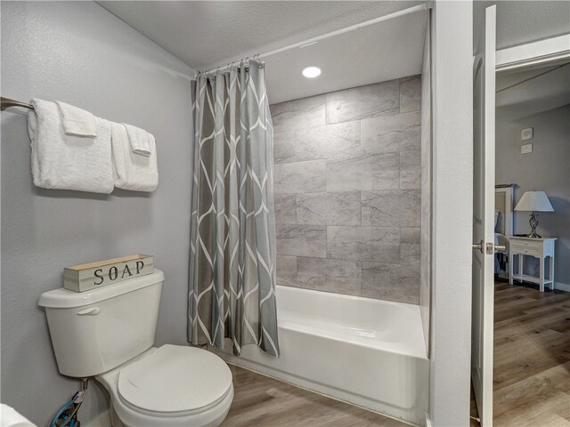 bathroom with hardwood / wood-style floors, a textured ceiling, shower / bath combo, and toilet