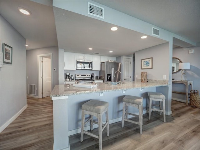 800 Sandcastle Dr Unit 129, Port Aransas, TX 78373 - kitchen with appliances with stainless steel finishes, a peninsula, light wood finished floors, a breakfast bar, and white cabinetry