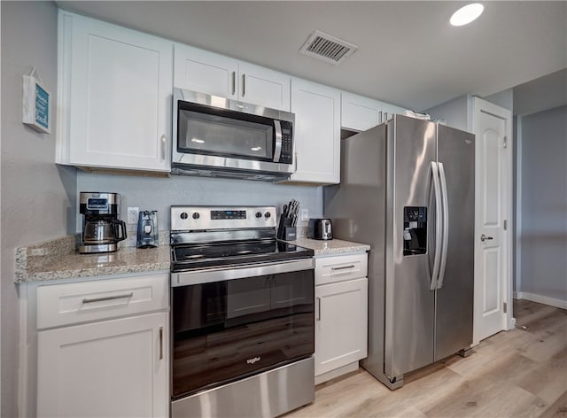 kitchen with white cabinets, light stone countertops, light wood-type flooring, and appliances with stainless steel finishes