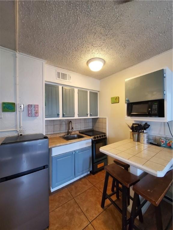 3938 Surfside Blvd Unit 1121, Corpus Christi, TX 78402 - kitchen with freestanding refrigerator, electric range oven, tile counters, blue cabinetry, and backsplash