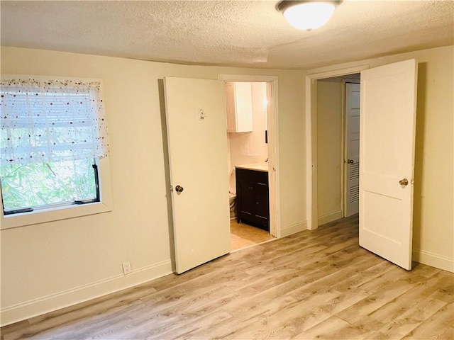 unfurnished bedroom featuring ensuite bathroom, light hardwood / wood-style floors, and a textured ceiling