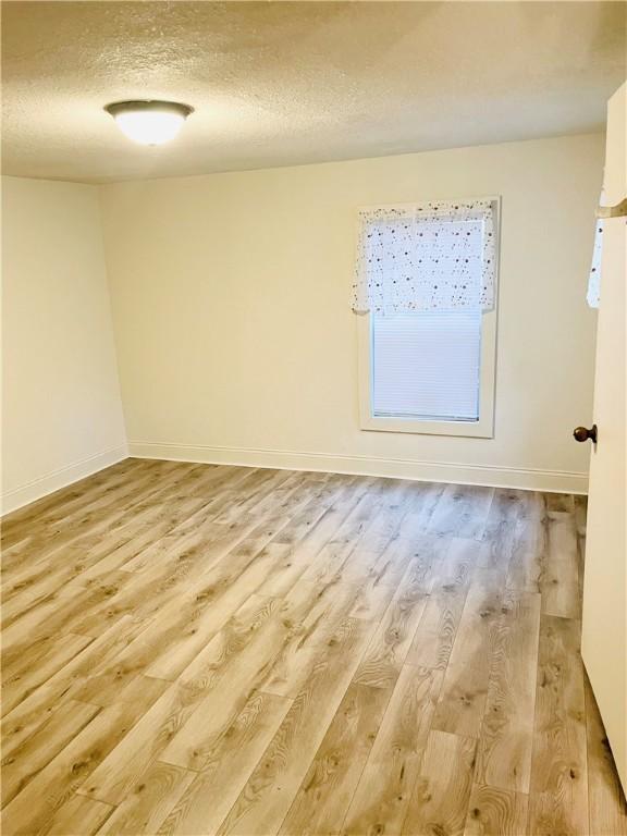 spare room with a textured ceiling and light hardwood / wood-style floors