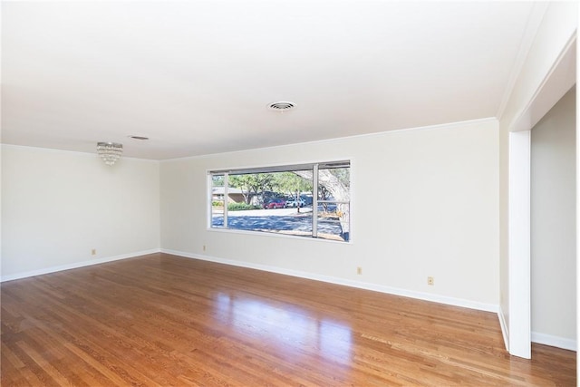 spare room featuring hardwood / wood-style flooring, crown molding, and a chandelier