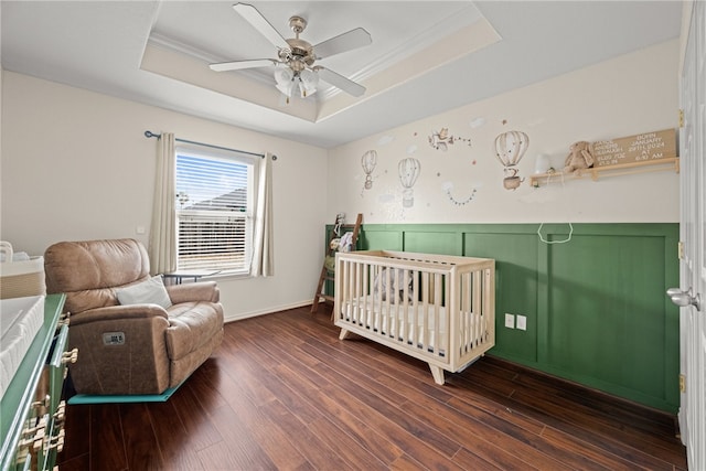 bedroom with a crib, dark hardwood / wood-style flooring, a tray ceiling, and ceiling fan