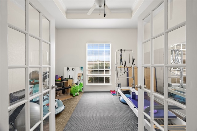 workout area with ceiling fan, french doors, ornamental molding, and a tray ceiling