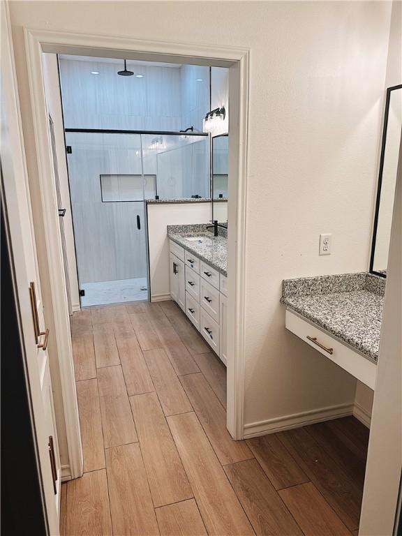 bathroom with baseboards, wood finish floors, vanity, and a stall shower