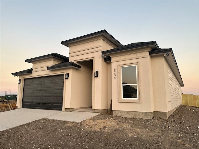 prairie-style house with driveway, an attached garage, fence, and stucco siding