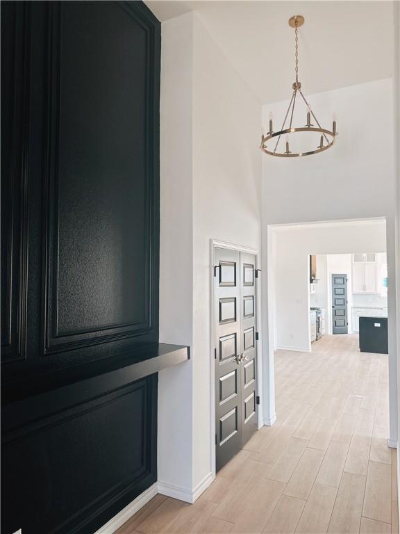 corridor featuring a towering ceiling, an inviting chandelier, baseboards, and wood finish floors