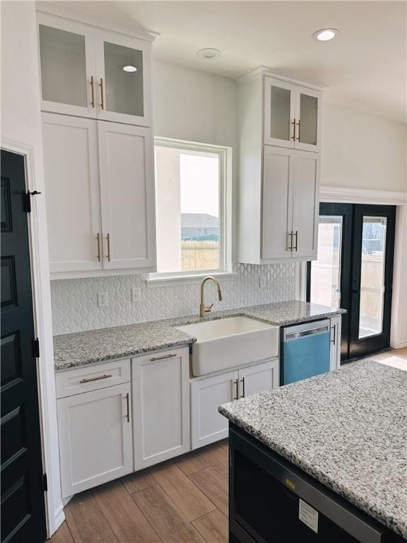 kitchen with tasteful backsplash, white cabinets, a sink, wood finished floors, and dishwashing machine