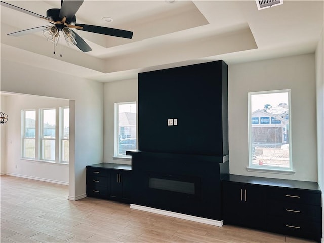 foyer featuring light wood-type flooring, plenty of natural light, visible vents, and a raised ceiling