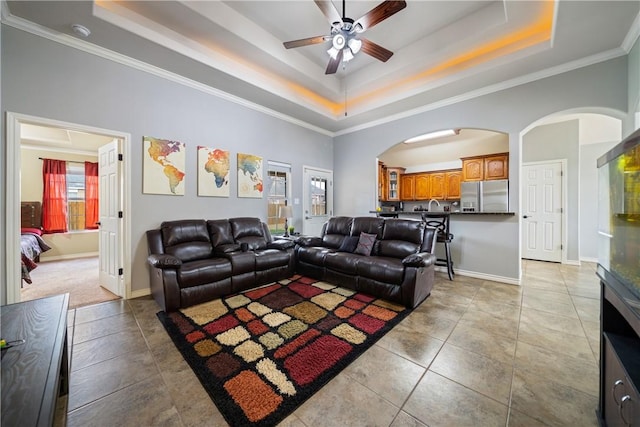 living room with light tile patterned flooring, crown molding, ceiling fan, a tray ceiling, and a towering ceiling