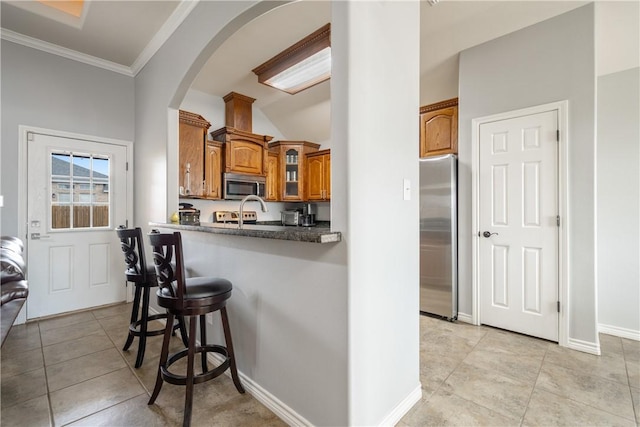 kitchen featuring light tile patterned floors, crown molding, a breakfast bar, appliances with stainless steel finishes, and kitchen peninsula