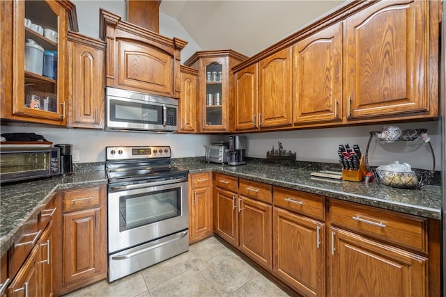 kitchen with lofted ceiling, stainless steel appliances, light tile patterned floors, and dark stone countertops