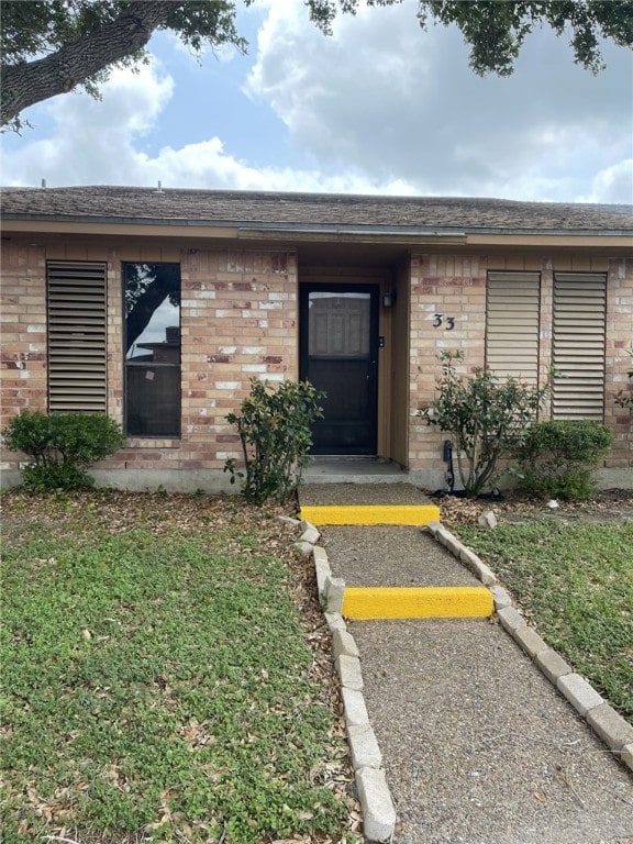 entrance to property featuring brick siding and a yard