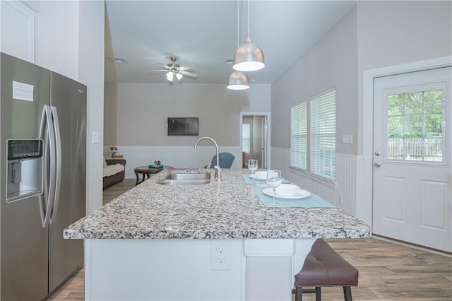 kitchen with decorative light fixtures, sink, stainless steel fridge, a kitchen island with sink, and light hardwood / wood-style flooring