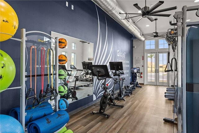 workout area featuring a ceiling fan, french doors, a towering ceiling, and wood finished floors