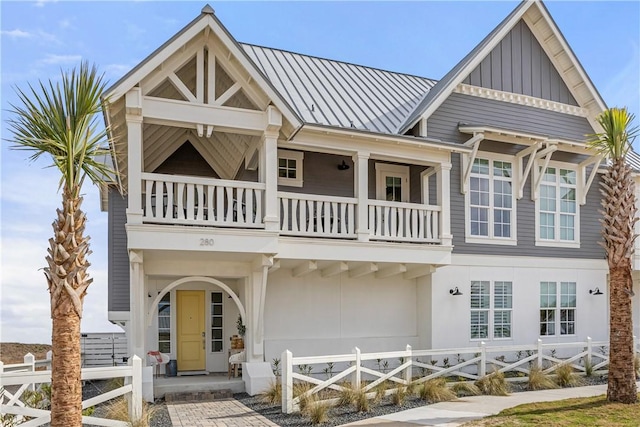 view of front facade with a fenced front yard, board and batten siding, a standing seam roof, metal roof, and a balcony