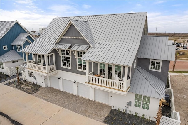 view of front facade featuring metal roof, an attached garage, a balcony, driveway, and a standing seam roof