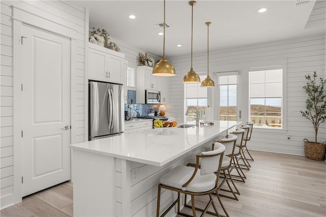 kitchen featuring appliances with stainless steel finishes, white cabinetry, light wood-style floors, and a kitchen bar