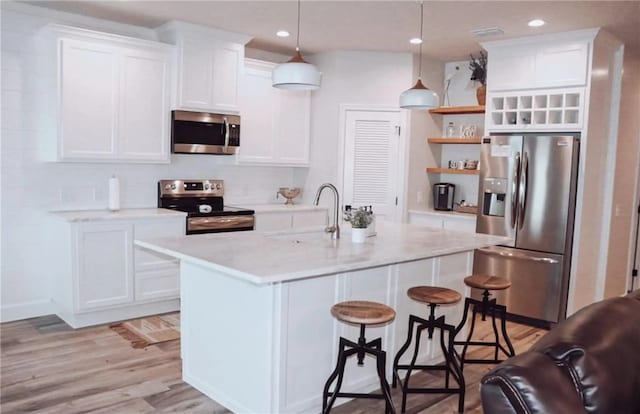  - kitchen featuring appliances with stainless steel finishes, a sink, open shelves, a breakfast bar, and light wood-type flooring
