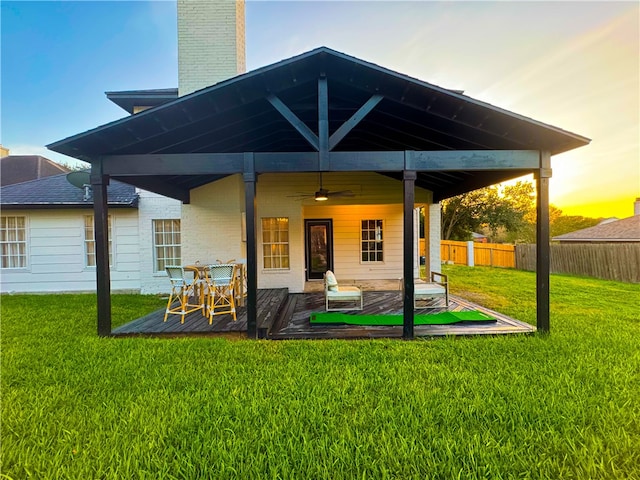 back house at dusk with a yard, ceiling fan, and a wooden deck