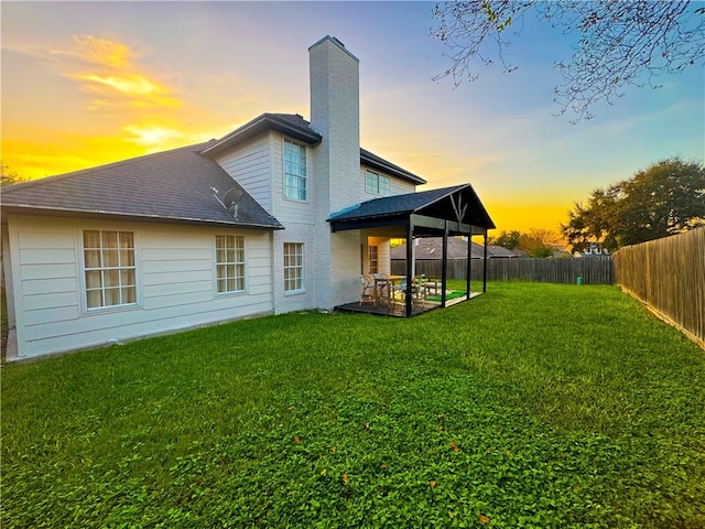 back house at dusk featuring a lawn and a patio area