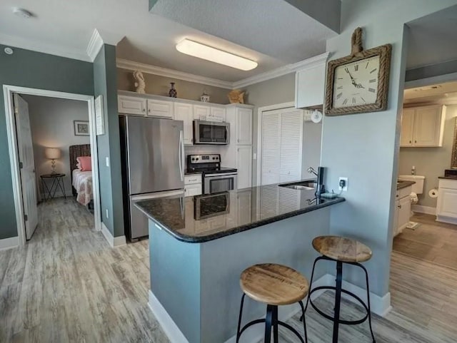 kitchen featuring light wood-style floors, appliances with stainless steel finishes, a peninsula, and white cabinetry