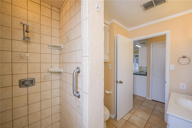 bathroom with tile patterned floors, toilet, a tile shower, ornamental molding, and vanity