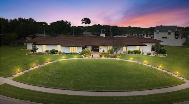 ranch-style house with a lawn, stucco siding, a chimney, and a tile roof