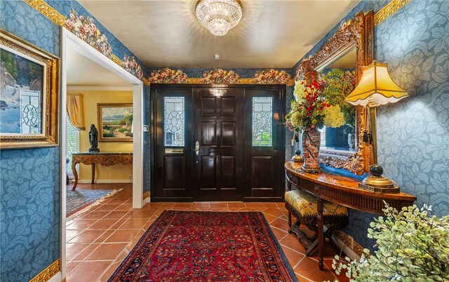 tiled entrance foyer featuring wallpapered walls, a notable chandelier, a wealth of natural light, and baseboards