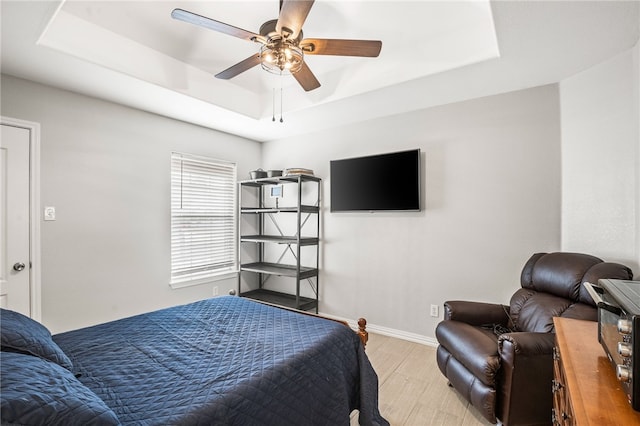 bedroom featuring light hardwood / wood-style flooring, ceiling fan, and a raised ceiling