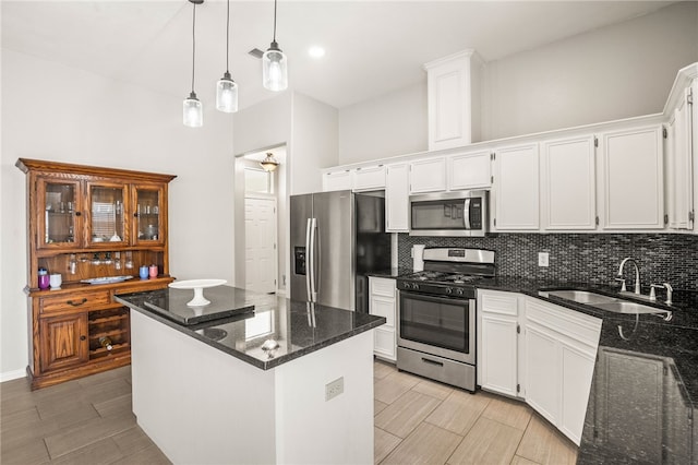 kitchen with stainless steel appliances, dark stone counters, sink, a kitchen island, and white cabinetry