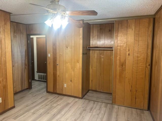10949 Gates Ln, Corpus Christi, TX 78410 - unfurnished bedroom featuring a closet, light wood-style flooring, a textured ceiling, wood walls, and ceiling fan