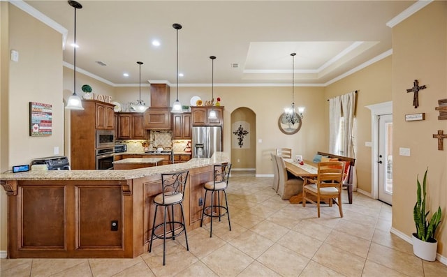 kitchen featuring crown molding, a breakfast bar area, stainless steel appliances, decorative backsplash, and a raised ceiling