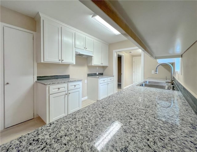 kitchen with white cabinets, light stone counters, and sink