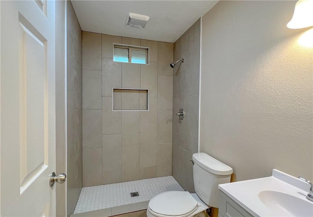 bathroom with a tile shower, vanity, and toilet