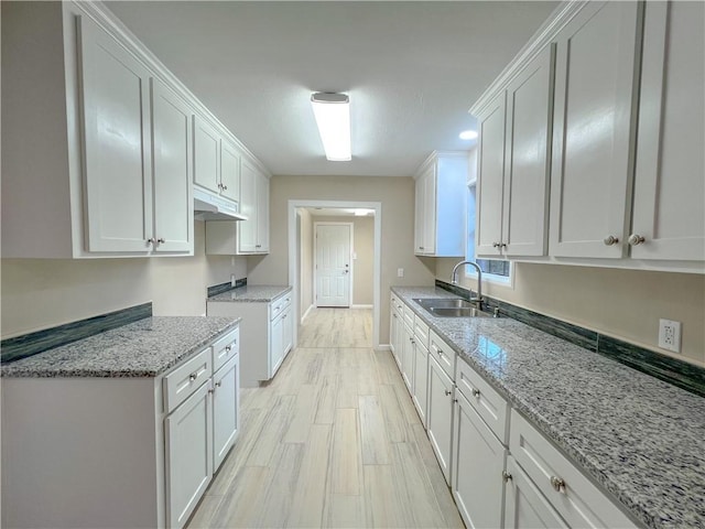 kitchen featuring white cabinets, light hardwood / wood-style flooring, light stone counters, and sink