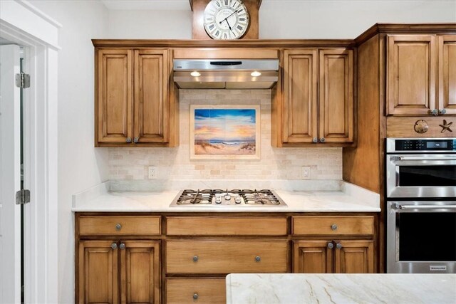 kitchen featuring stainless steel double oven, range hood, gas stovetop, and backsplash