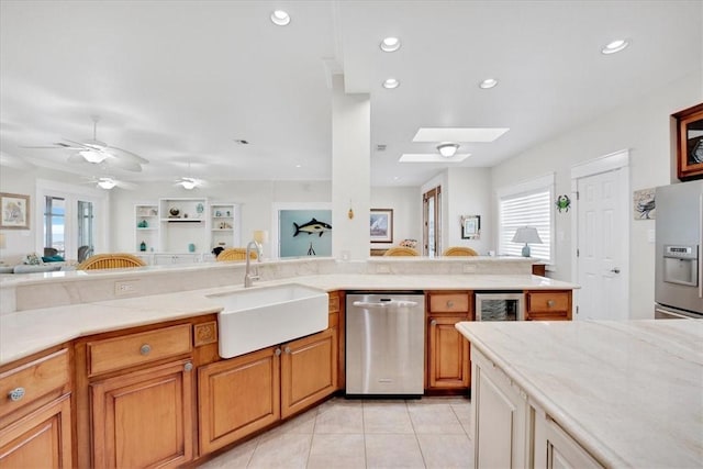 kitchen featuring sink, stainless steel appliances, light tile patterned flooring, ceiling fan, and a skylight