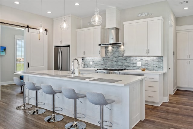 kitchen with stainless steel appliances, white cabinetry, a barn door, dark wood-type flooring, and a kitchen island with sink